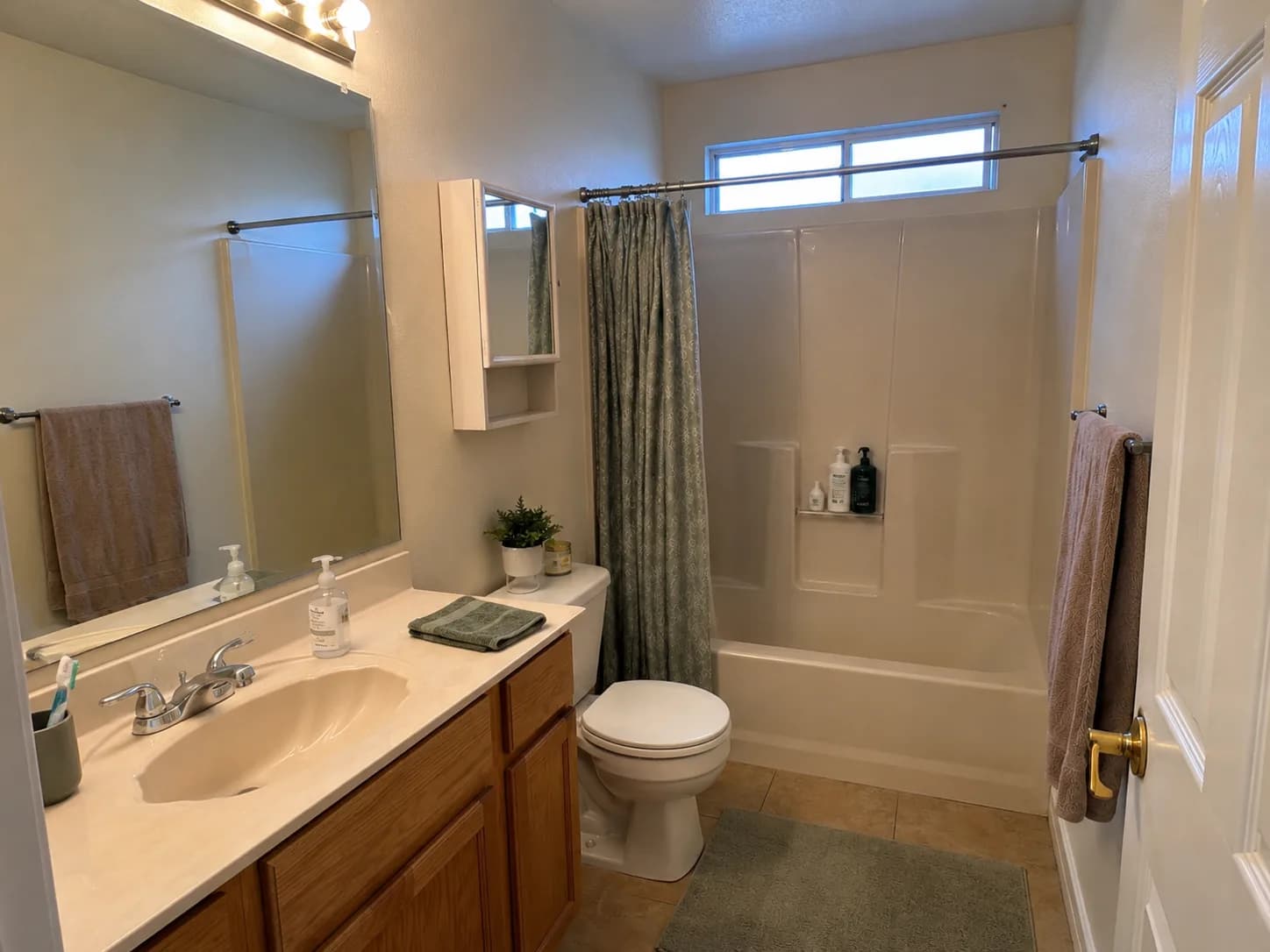 A dated bathroom: cultured-marble vanity with oak cabinets, a fibreglass tub surround, and a shower curtain.
